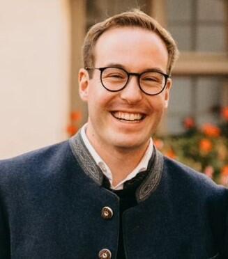 Alexander Grotz mit Brille und Trachtenjacke vor blühendem Hintergrund.