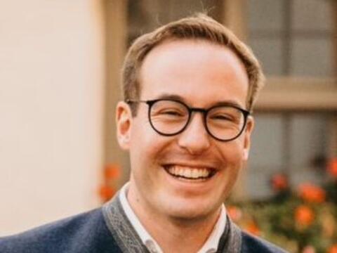 Alexander Grotz mit Brille und Trachtenjacke vor blühendem Hintergrund.